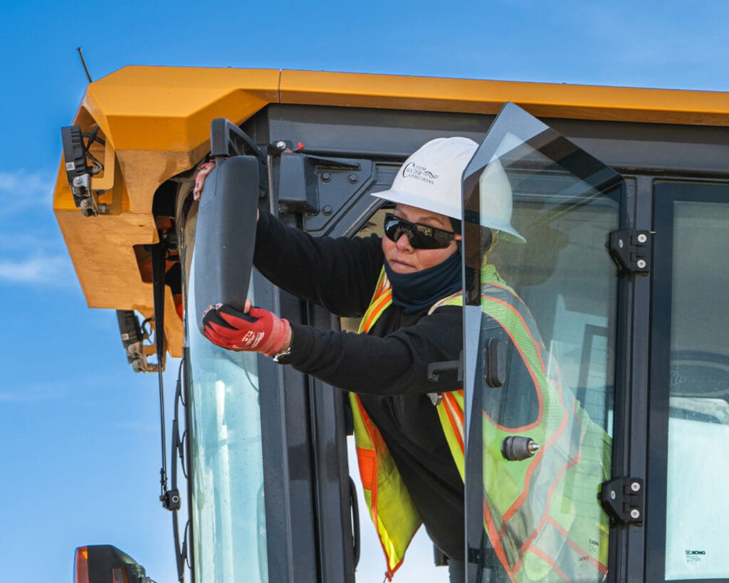 A professional technician in safety gear conducting a close inspection of a critical machine part (engine or hydraulics) or reviewing maintenance records on a tablet.