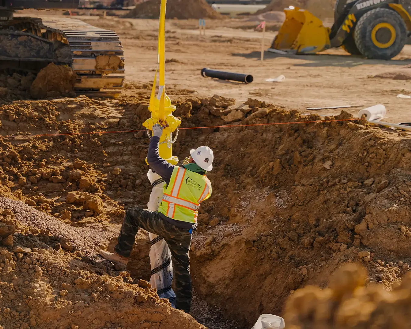 Construction worker using a safety harness inside a trench on an active jobsite, emphasizing the importance of equipment reliability and safe operations.